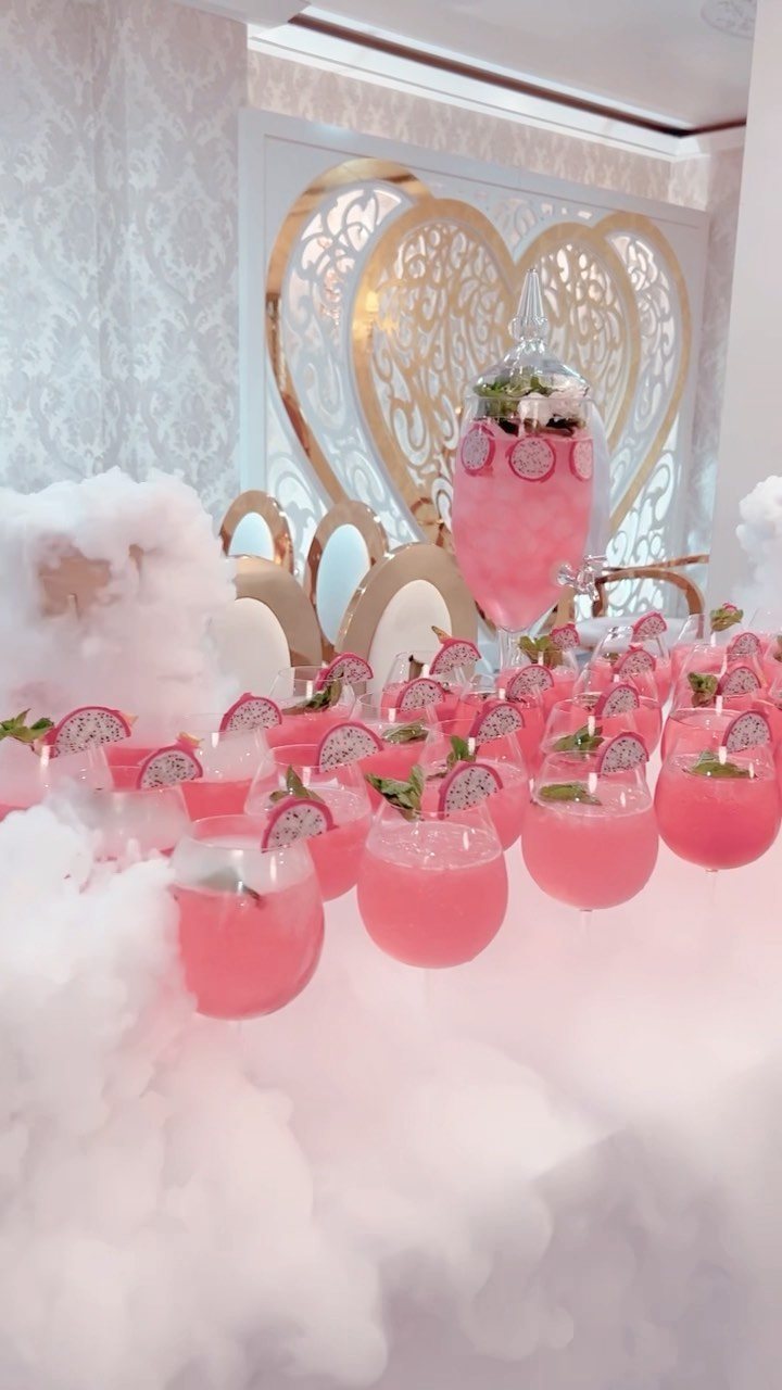 Pink cocktails with fruit garnishes arranged on a table surrounded by thick white dry ice smoke.