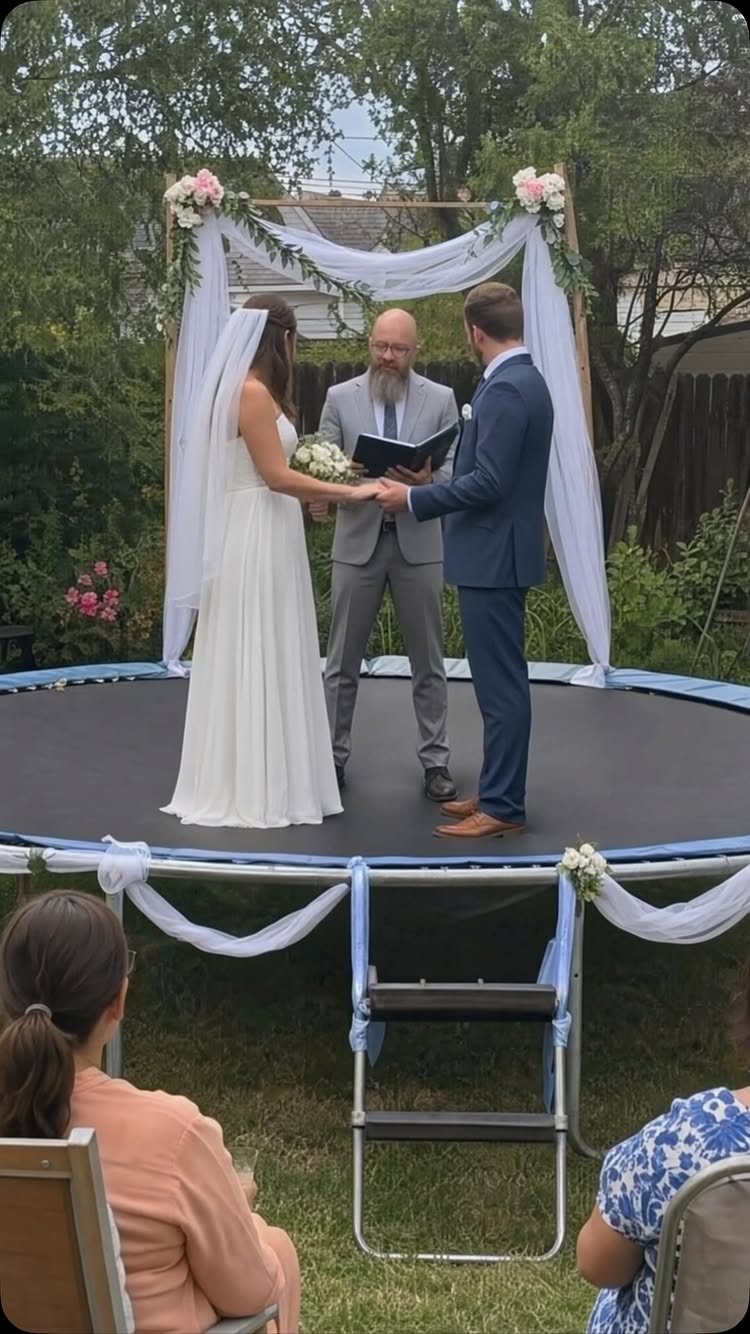 A bride and groom exchange vows while standing on a trampoline during an outdoor wedding ceremony.