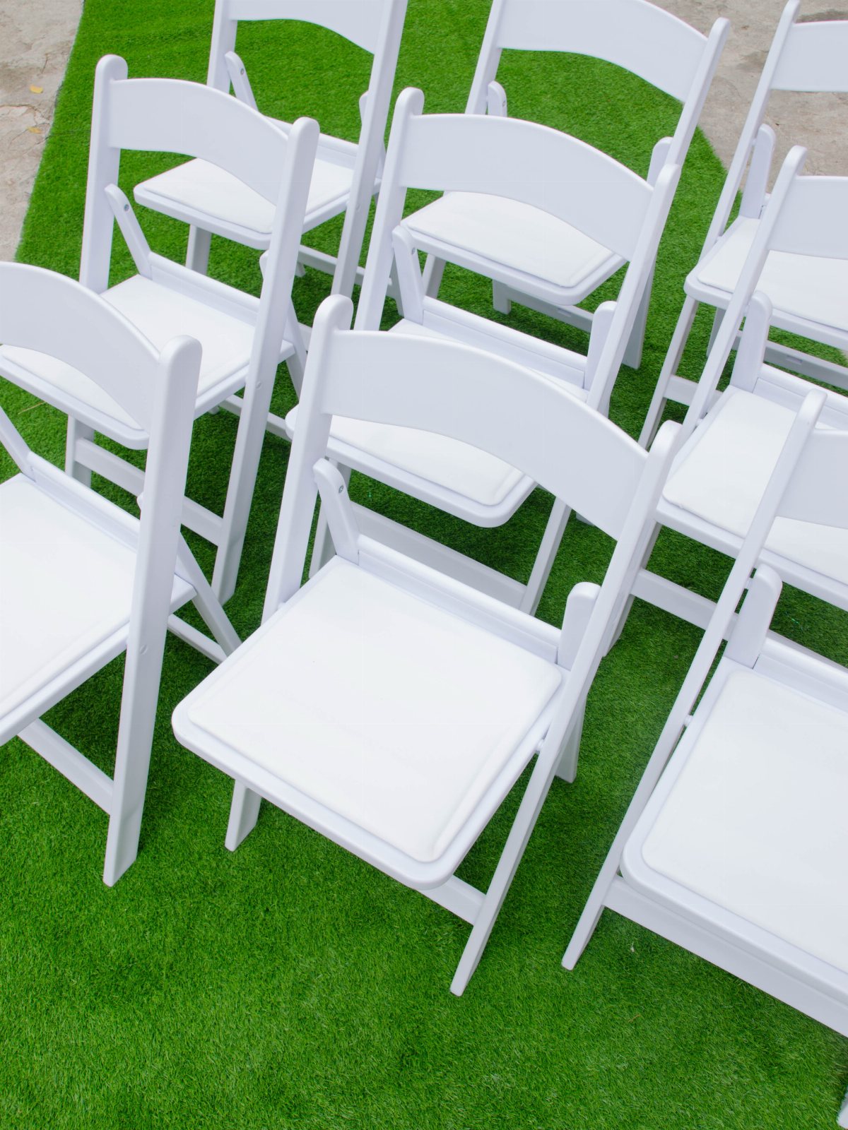 White plastic folding chairs arranged in rows on bright green artificial grass.
