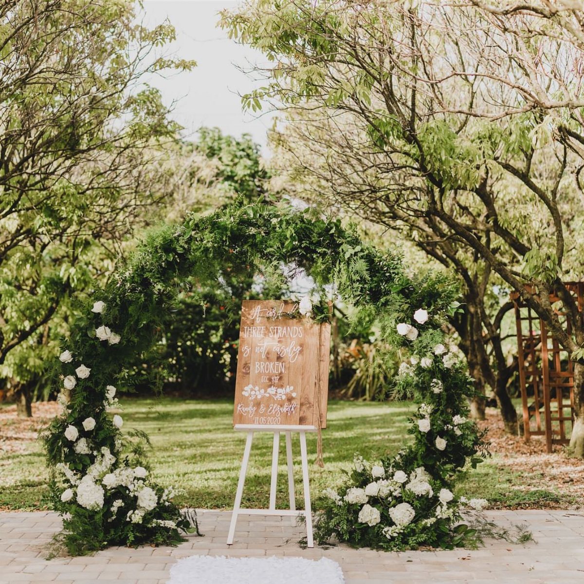 A circular wedding arch decorated with green leaves and white flowers in a garden.