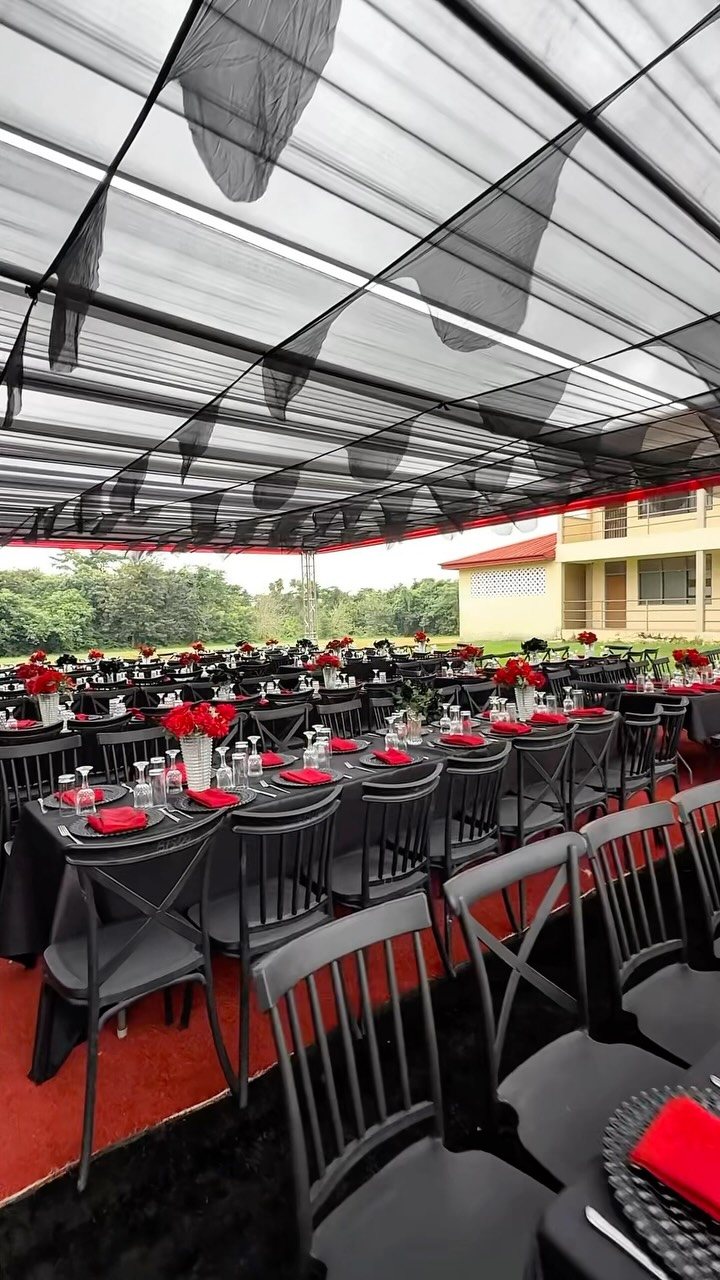 Dining tables set with black linens, red napkins, and red floral arrangements under a canopy.