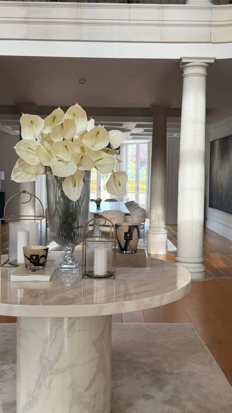 White anthurium flowers in a glass vase with candle lanterns on a marble table.