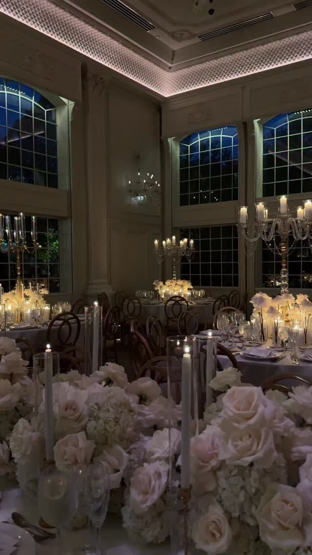White rose centerpieces and silver candelabras on elegant wedding reception tables in a ballroom.