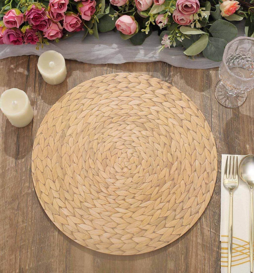 A woven straw placemat on a wooden table decorated with pink roses and greenery.