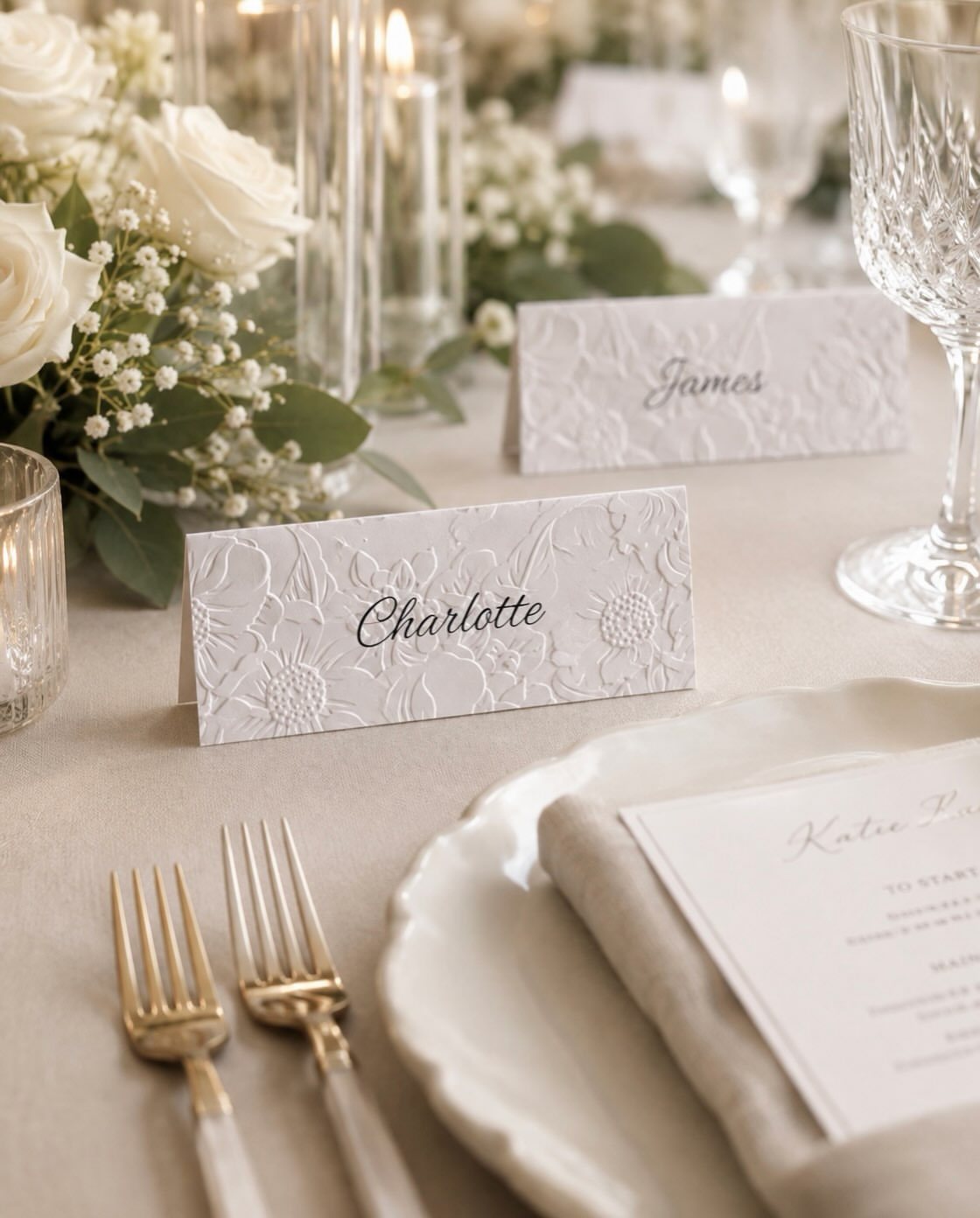 White floral place cards with names Charlotte and James on an elegant wedding table setting.