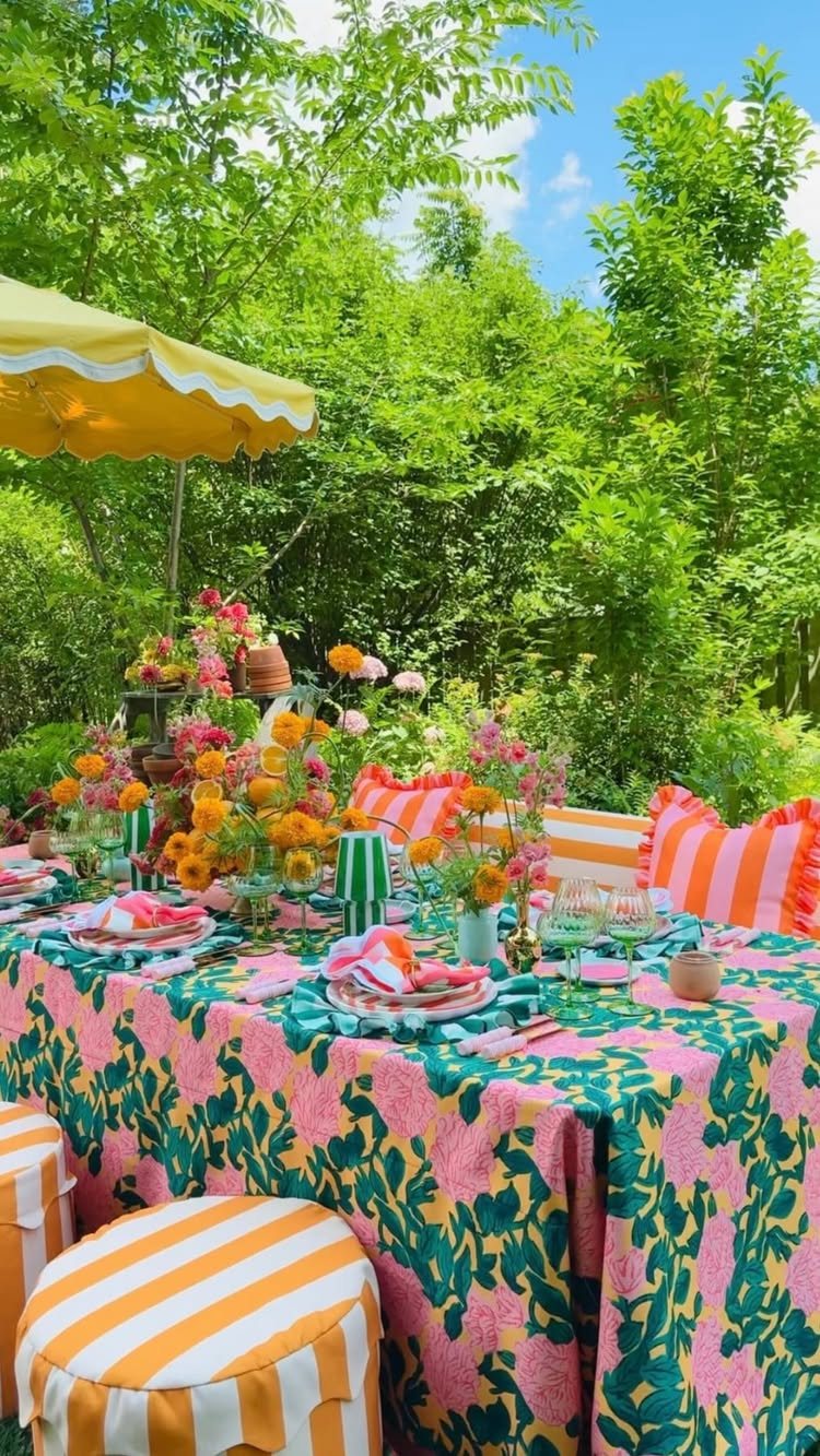 A colorful outdoor table set with bright floral patterns, orange flowers, and striped cushions in a garden.