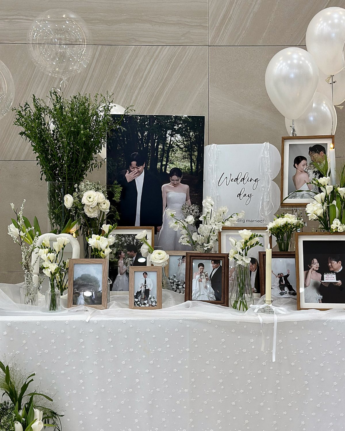 Framed wedding photographs and white flowers arranged on a white tablecloth with balloons.