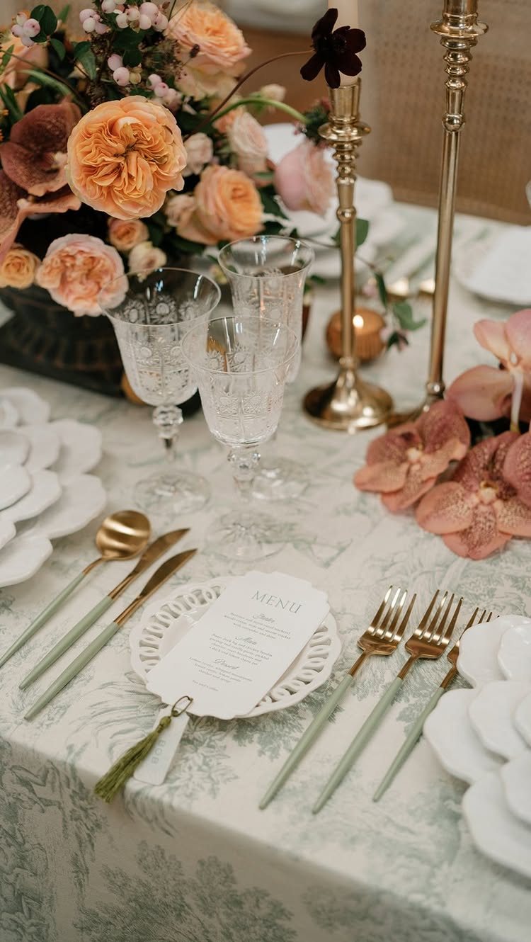 Elegant wedding table setting with patterned linens, peach roses, gold cutlery, and crystal glassware.