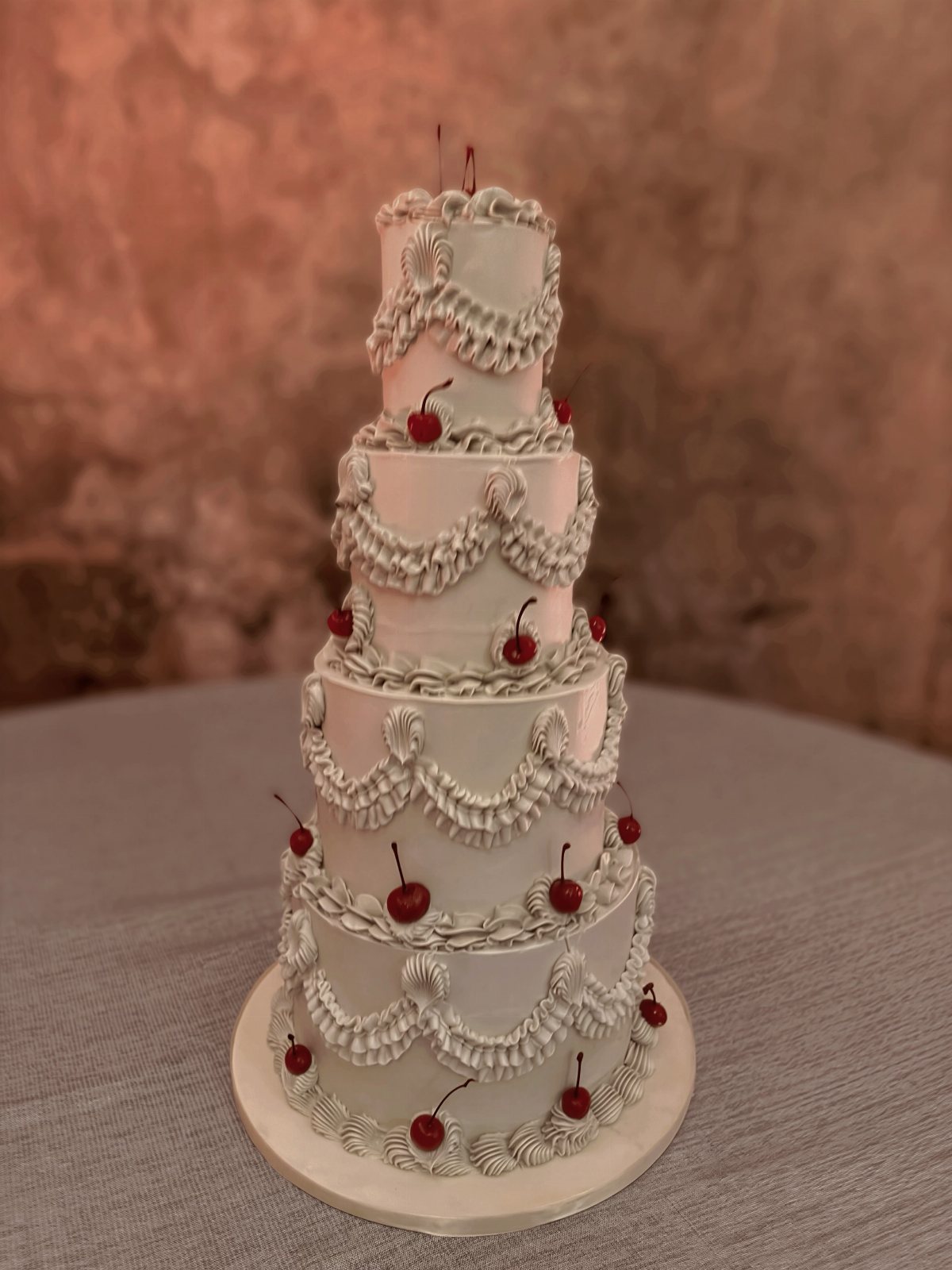 Four-tier white frosted cake decorated with piped buttercream swirls and bright red cherries.