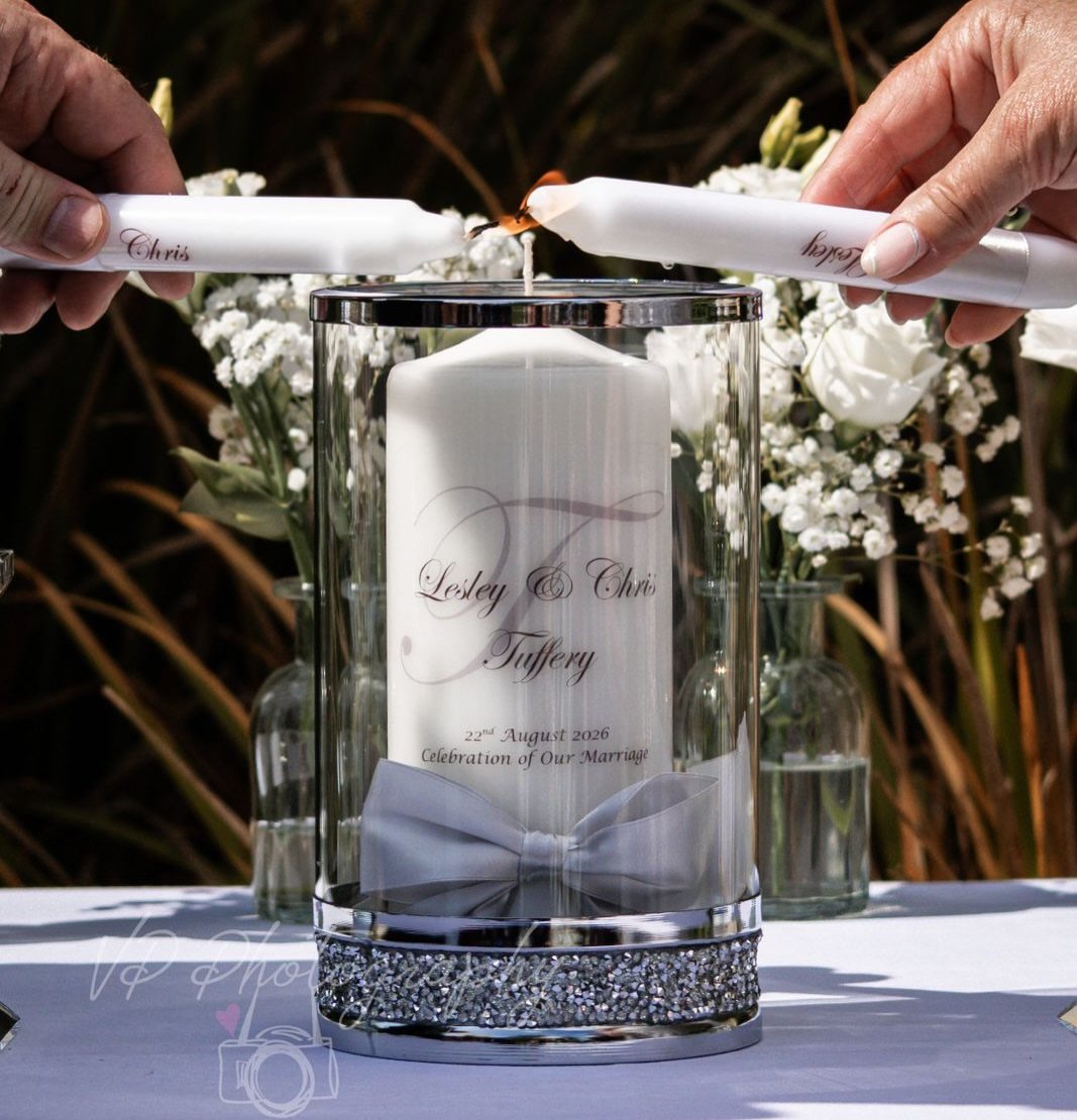 Two hands bring lit taper candles together to light a large central pillar candle.