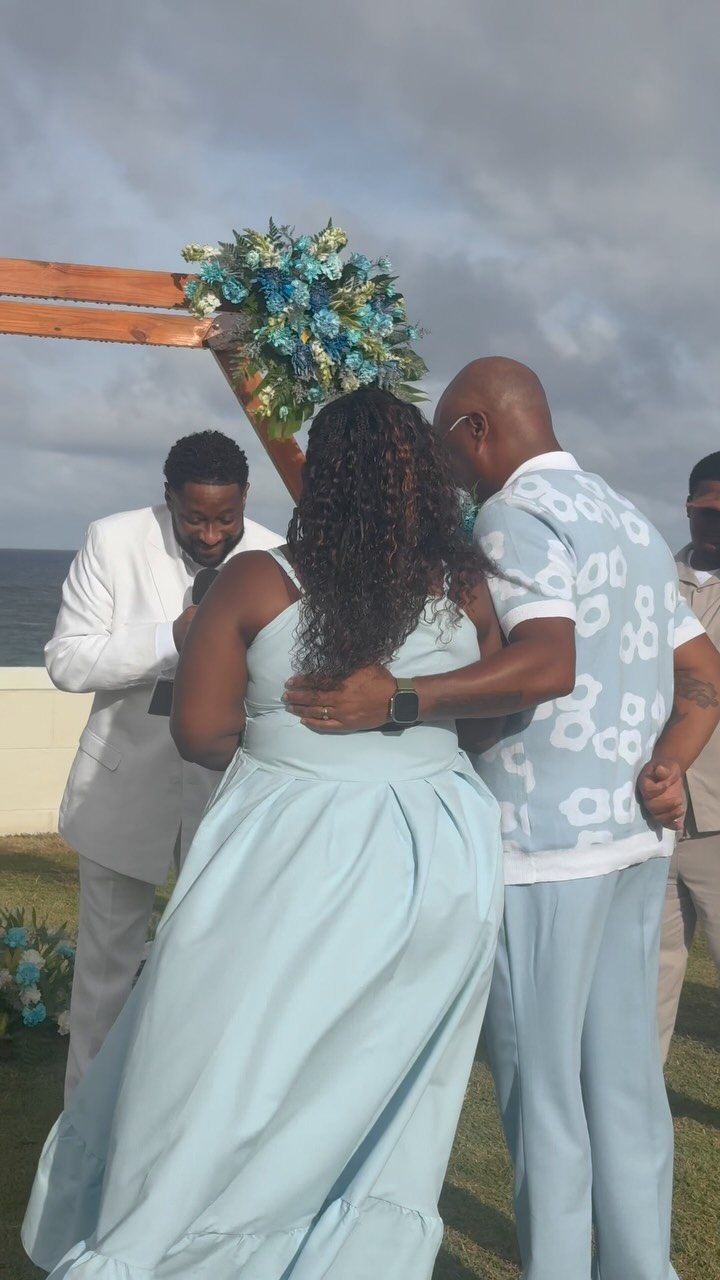 A man in a white suit surprises a woman wearing a light blue dress outdoors.
