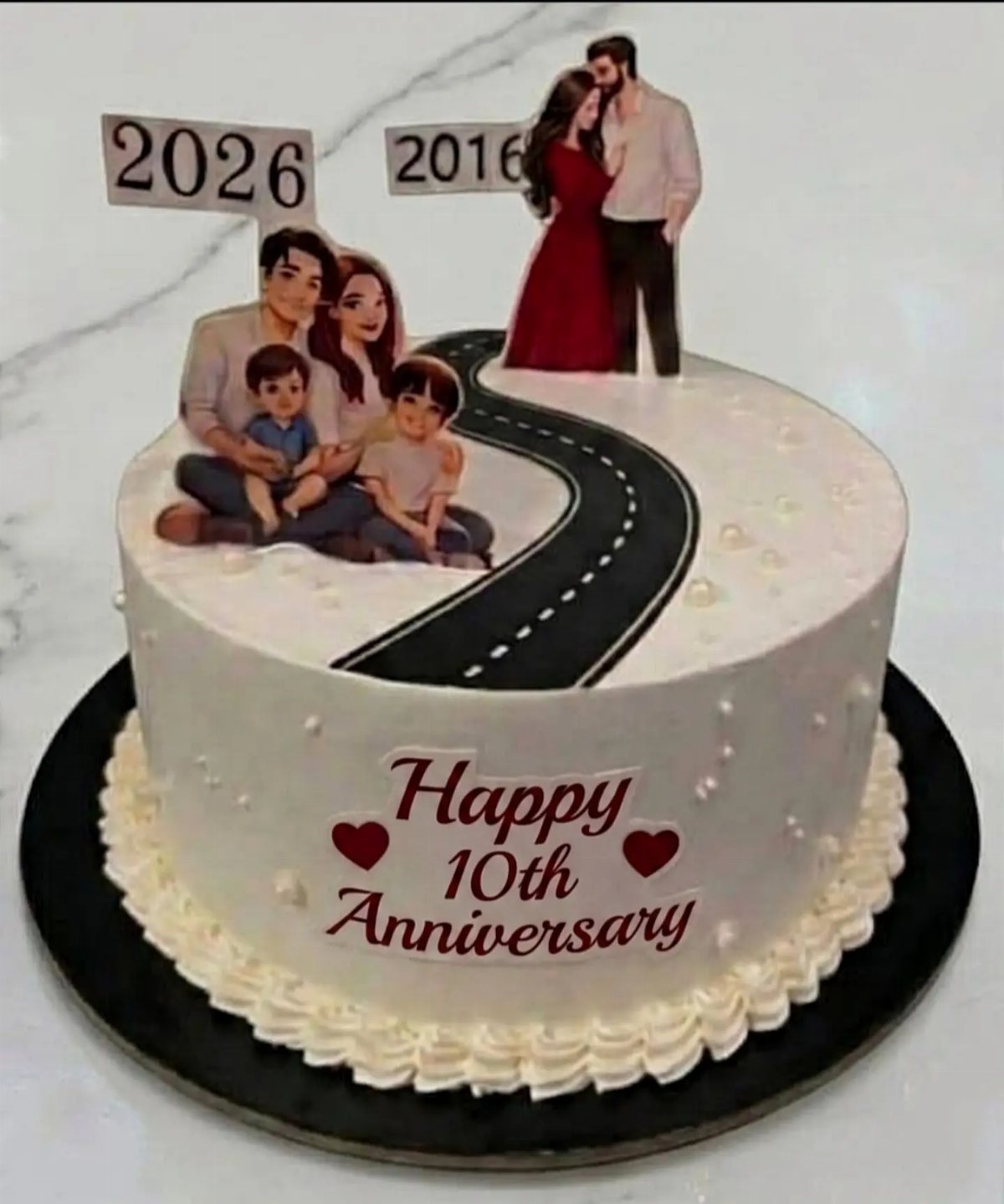 A white anniversary cake featuring family cutouts, a winding road, and text celebrating a 10th anniversary.