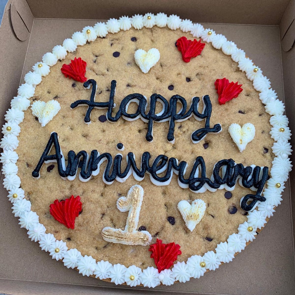 Chocolate chip cookie cake decorated with white frosting, red hearts, and black anniversary lettering.