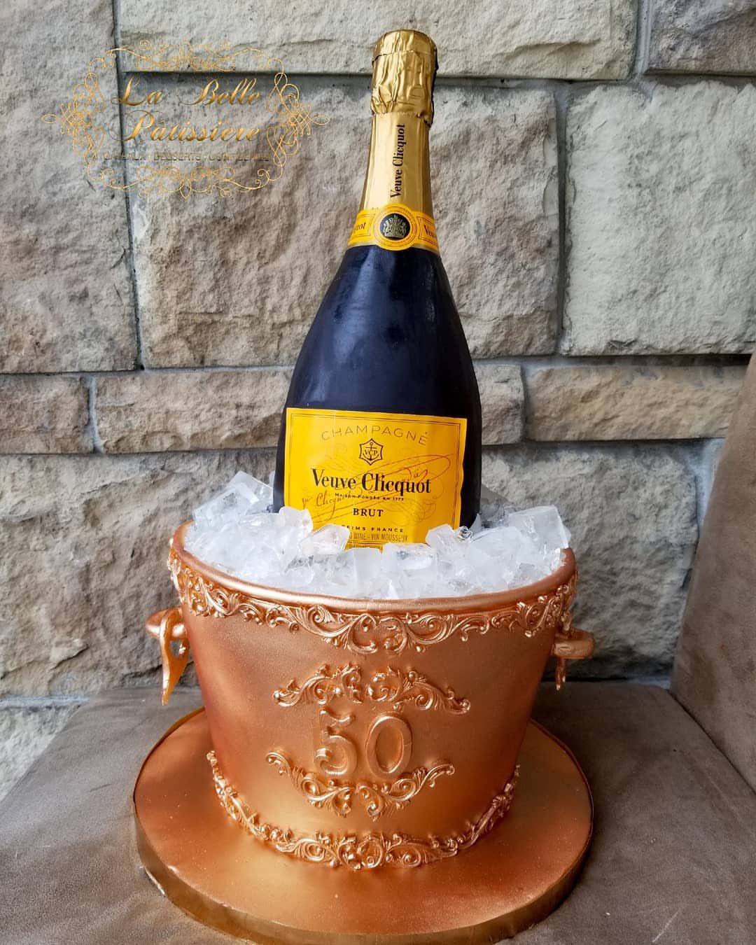 Champagne bottle in an ice bucket shaped like a gold decorative cake with number 50.