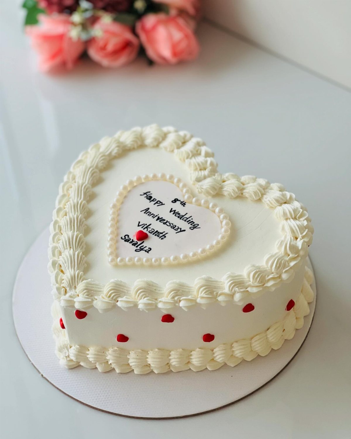 A white heart-shaped cake with red heart accents and piped cream borders on a white surface.