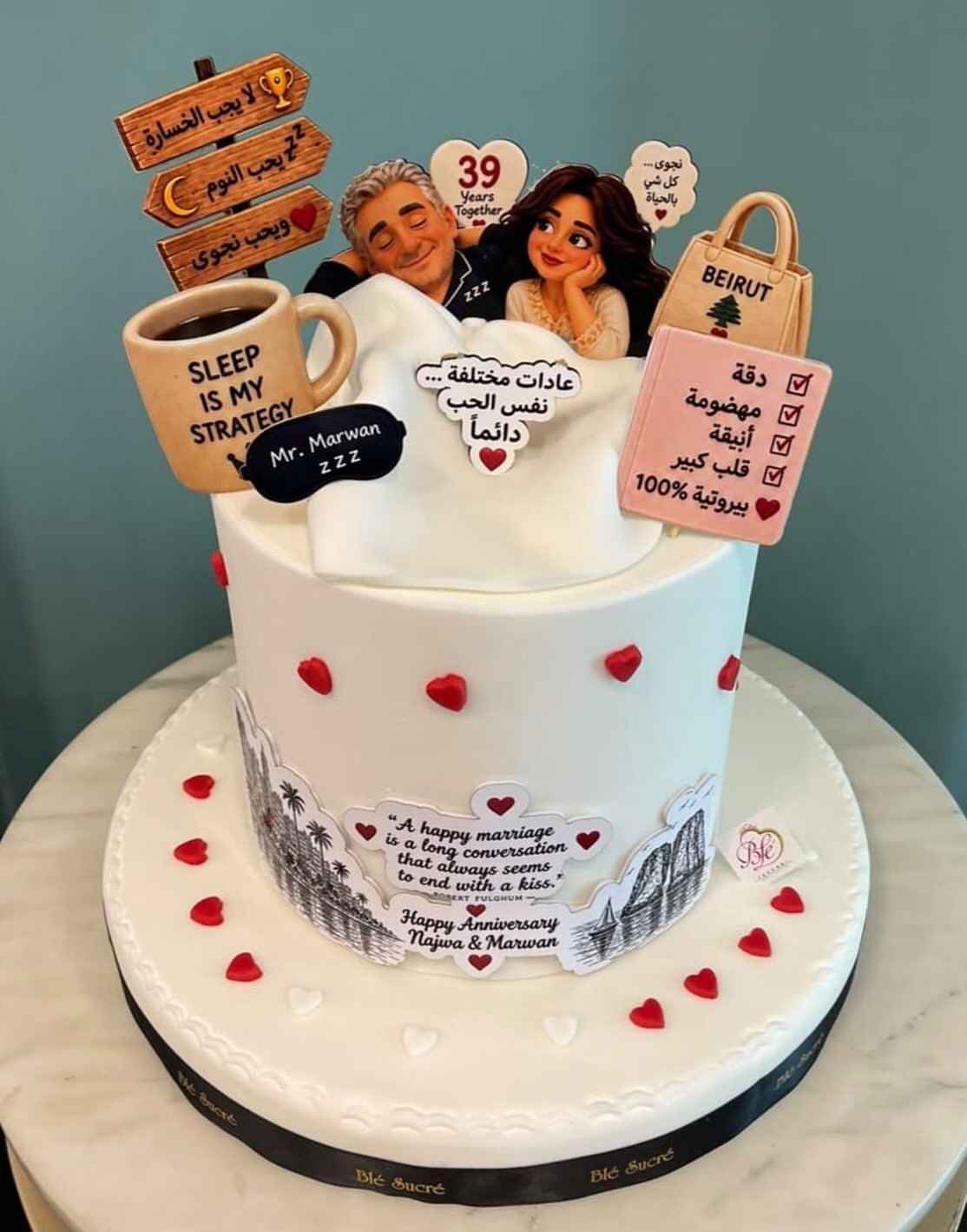 White anniversary cake decorated with red hearts and various personalized edible caricature toppers.