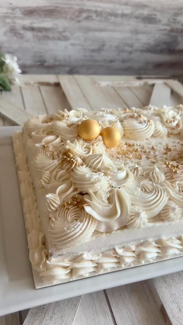 Rectangular sheet cake with white buttercream swirls and gold decorative spheres on a white platter.