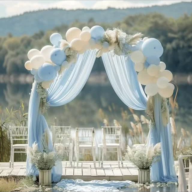 Light blue chiffon fabric draped over a wedding arch decorated with white and blue balloons.