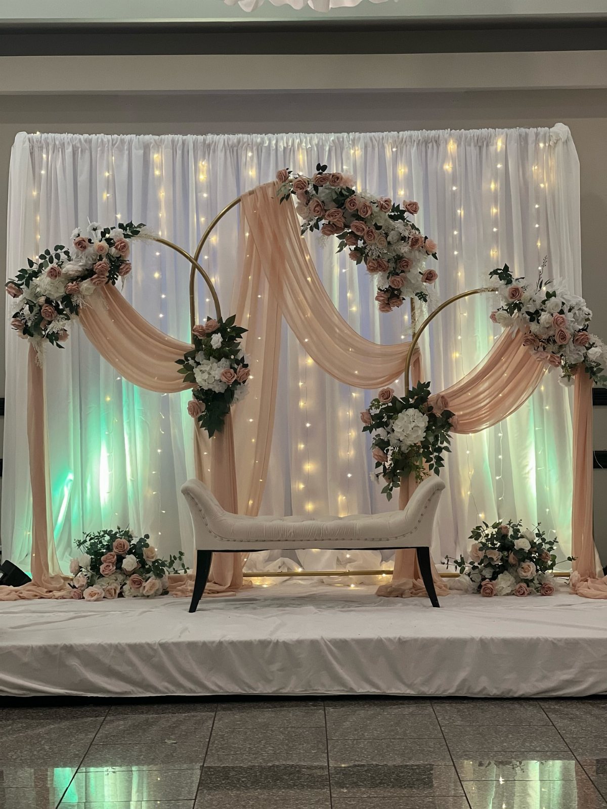 Gold circular wedding arch with peach fabric draping and white and pink floral arrangements.