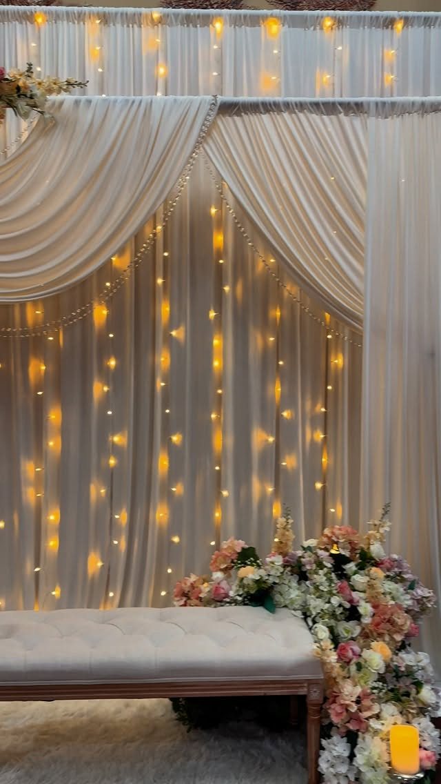 White sheer fabric draped over an arch with warm string lights glowing behind the curtains.