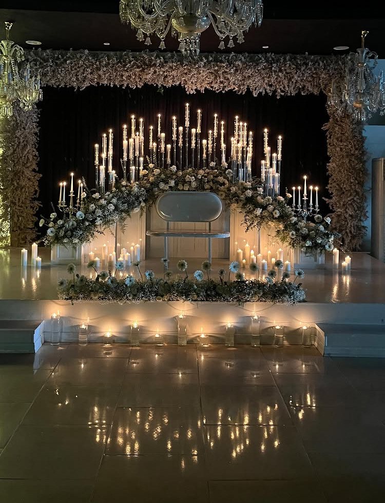White floral archway illuminated by many tall, glowing candles in a dark indoor setting.