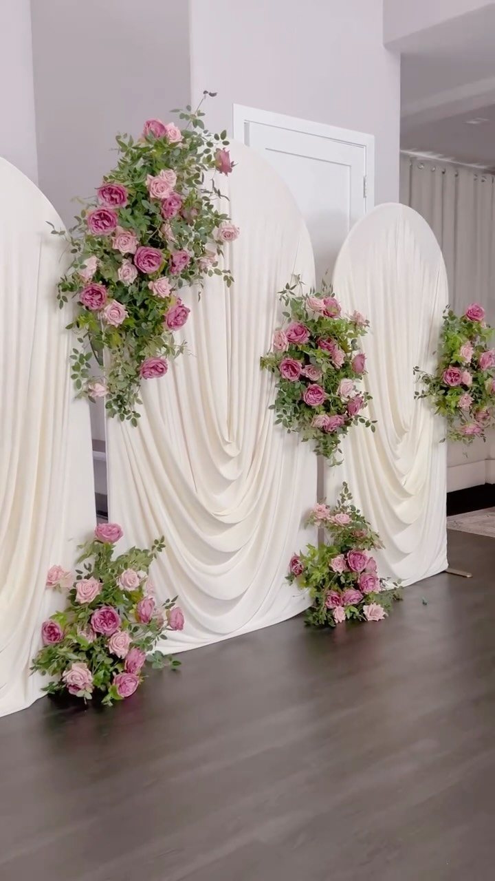 White draped fabric arches decorated with pink roses and green leaves on a dark floor.