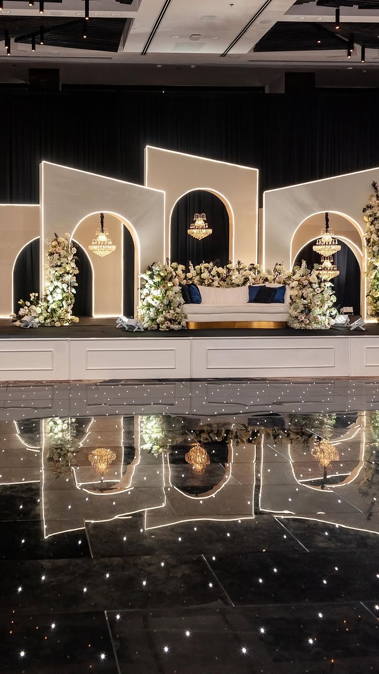 Cream geometric wedding arches with LED outlines and white floral arrangements on a stage.