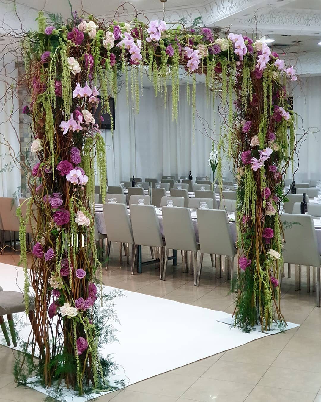 A floral wedding arch made of branches and pink flowers standing in a banquet hall.
