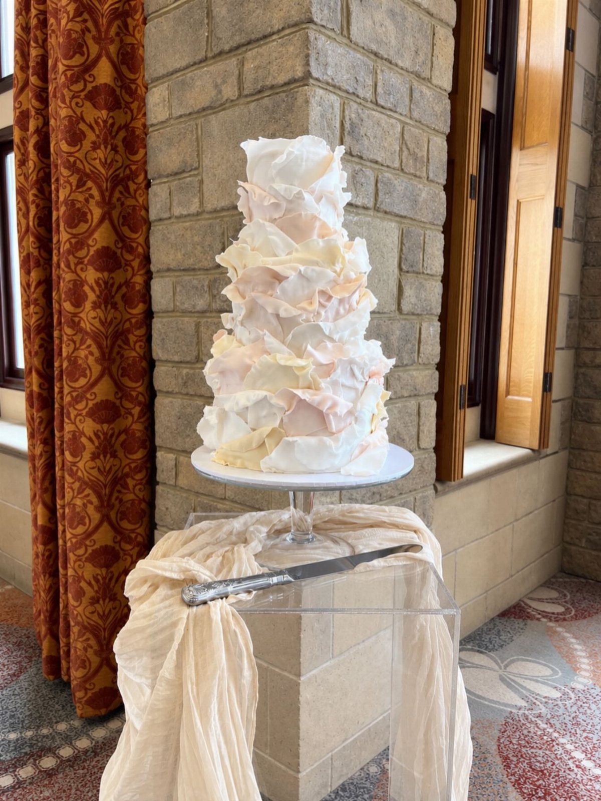A three-tier wedding cake covered in soft pink and white fondant ruffles on a pedestal.
