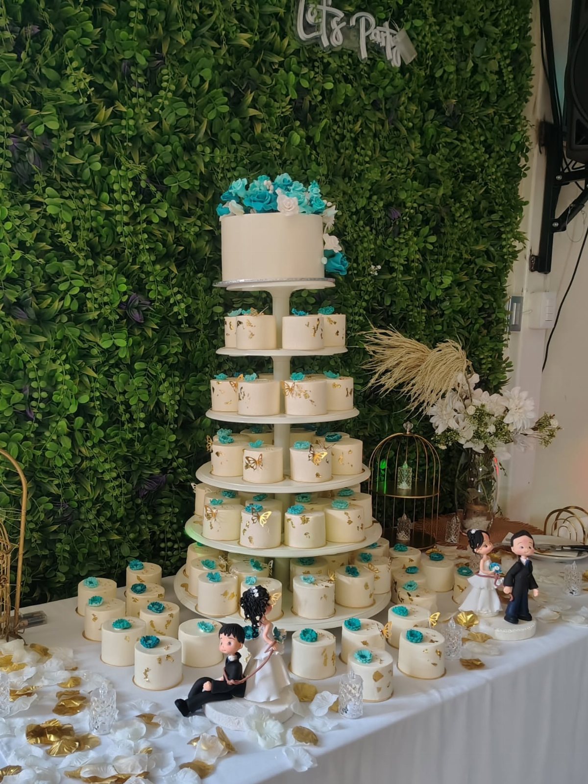 Tiered white cupcakes with blue floral accents and gold leaf on a white table.