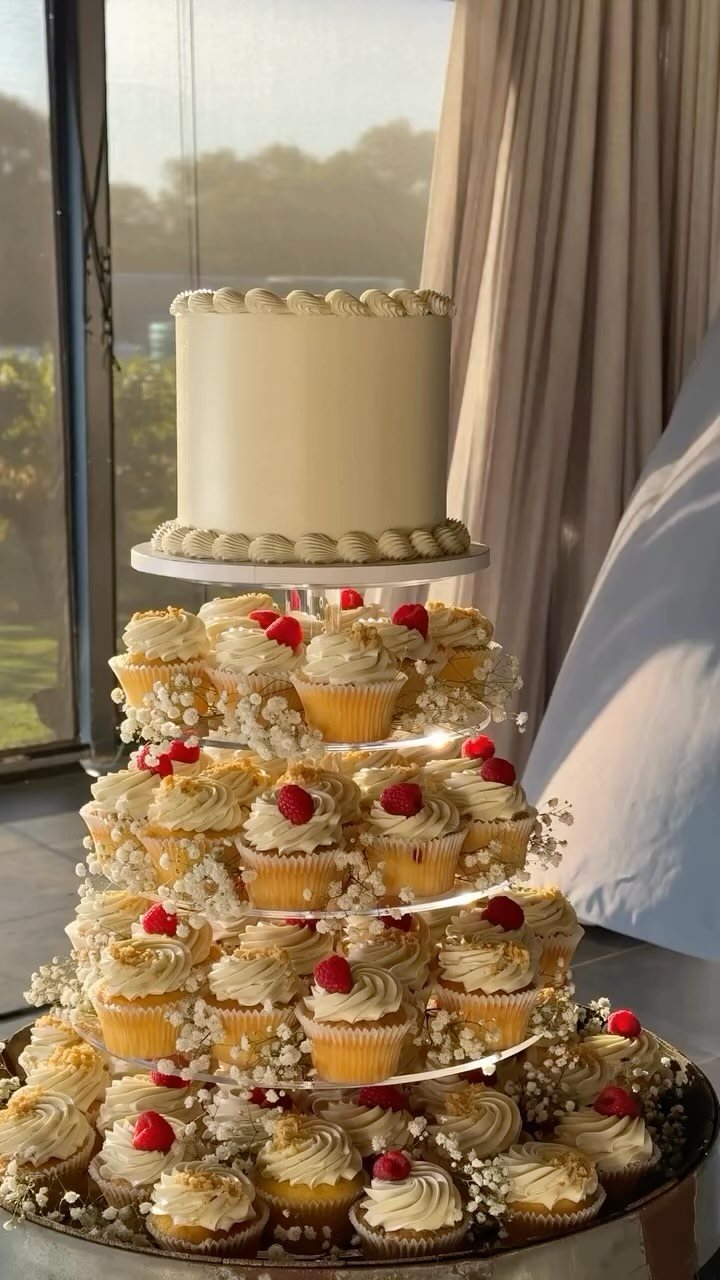 A tiered cupcake stand topped with a small cream cake and decorated with red berries.