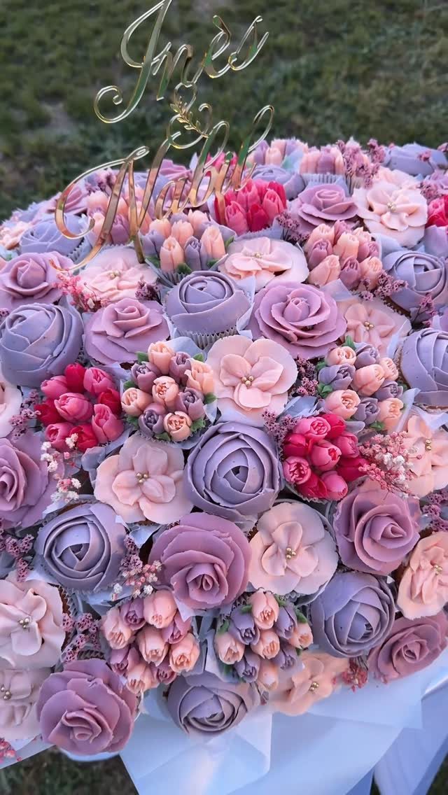 Floral cupcakes in lavender and pink tones arranged with a gold script cake topper.