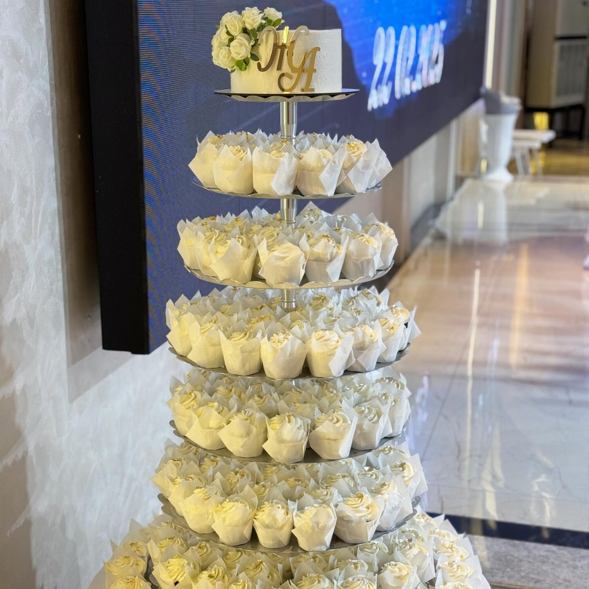 A tiered cupcake stand topped with a small white wedding cake and white roses.