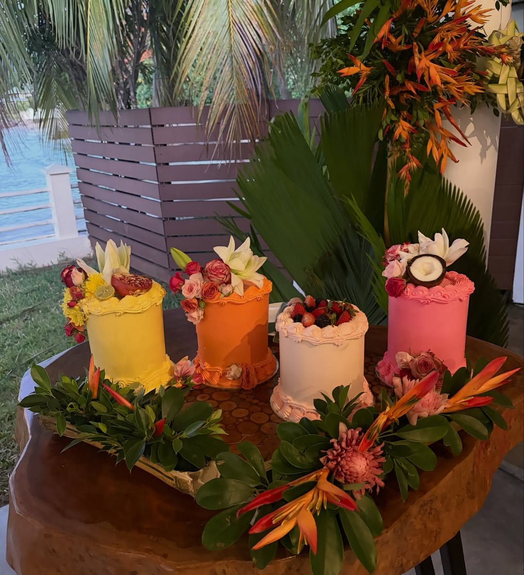 Four colorful small cakes decorated with fresh tropical fruits and flowers on a wooden table.