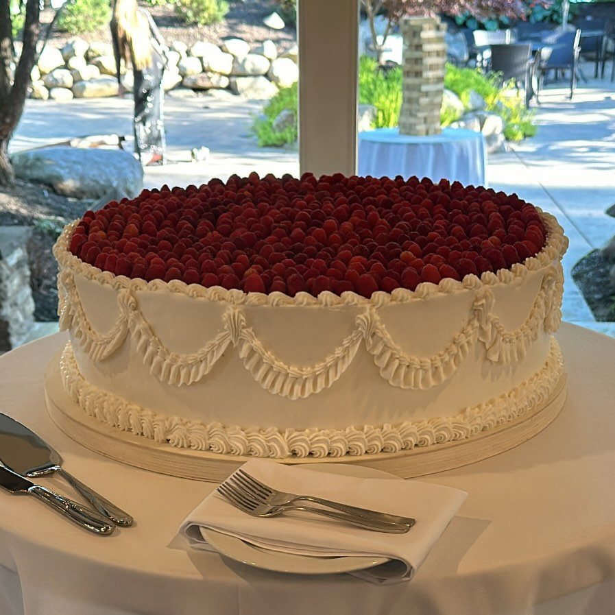 A white frosted cake topped with a thick layer of fresh red raspberries on a table.