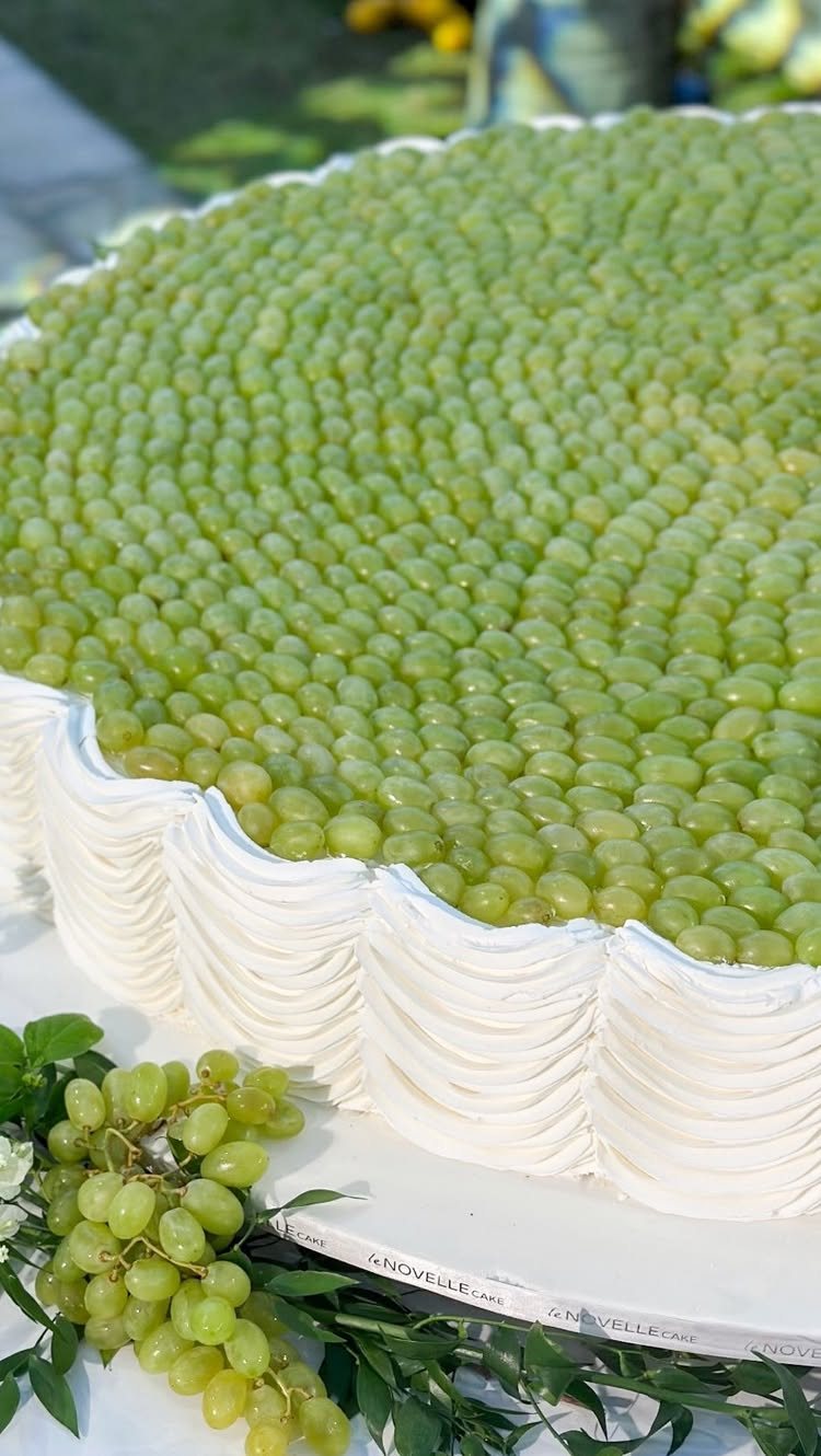 A large cake topped with a dense layer of small green grapes and white frosting.