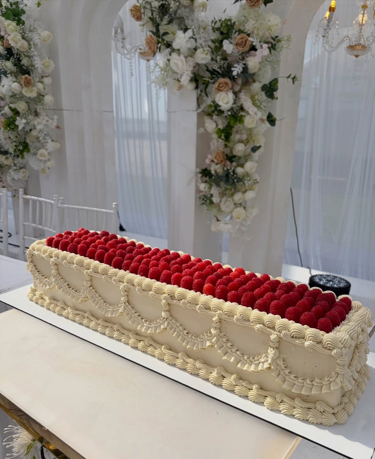 A long rectangular cream cake topped with a thick layer of fresh red raspberries.