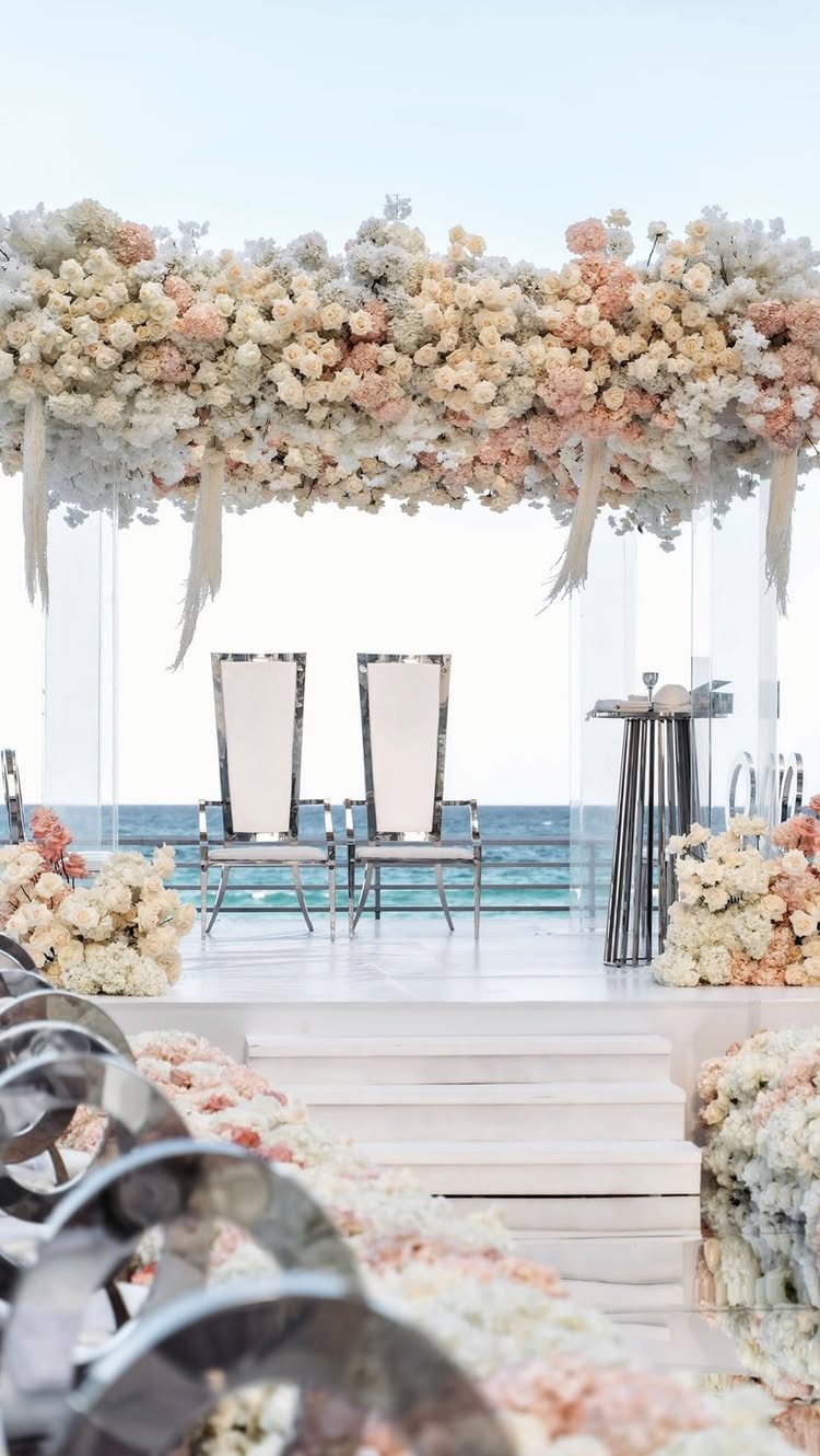 Floral canopy of peach and white flowers hanging over a white wedding altar by the sea.
