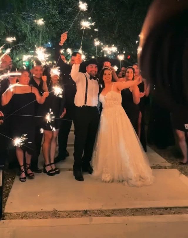 Bride and groom posing with wedding guests holding glowing sparklers at night.