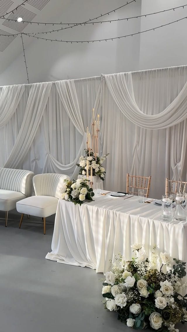 White fabric draperies hung in elegant swags behind a decorated wedding head table.