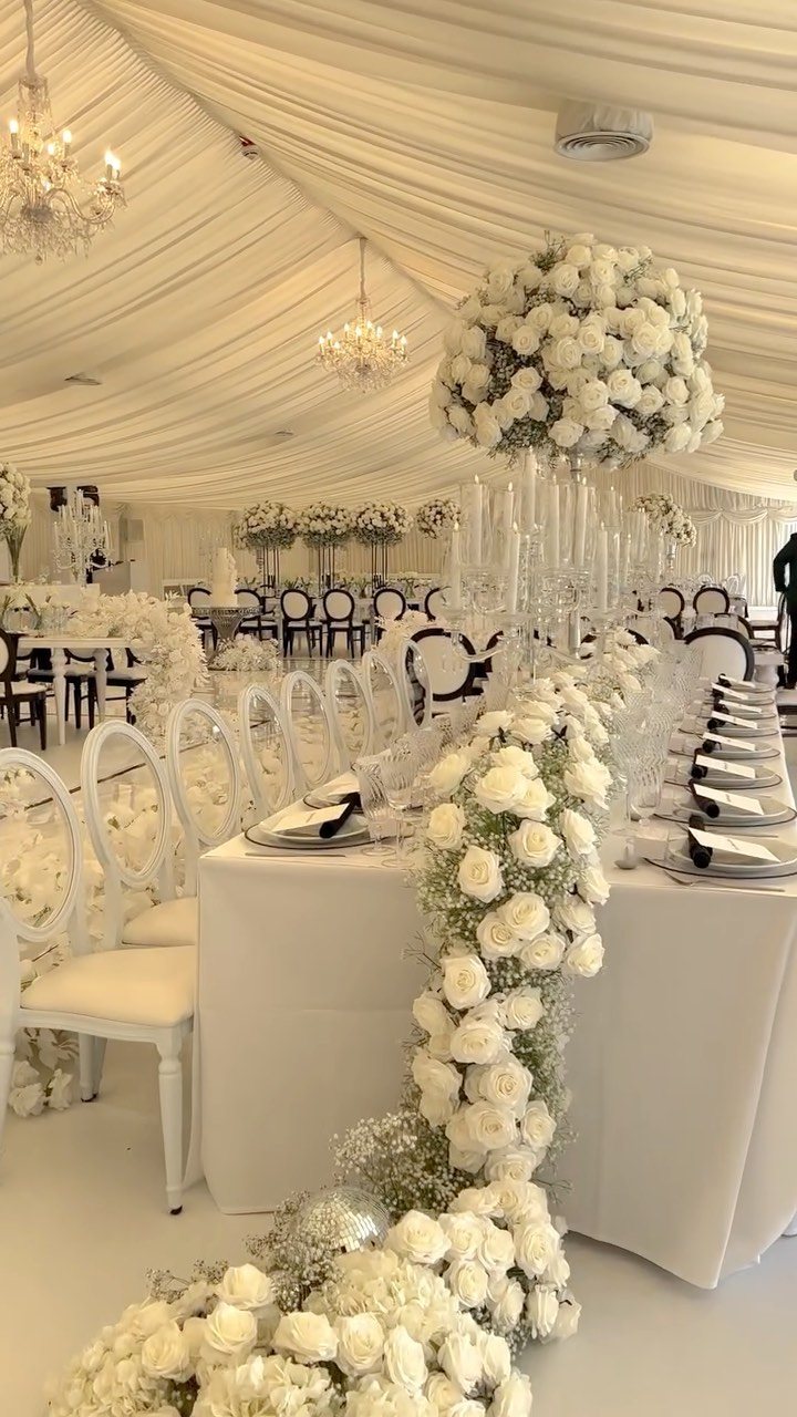 White wedding table decorated with cascading white rose garlands and tall glass candle holders.