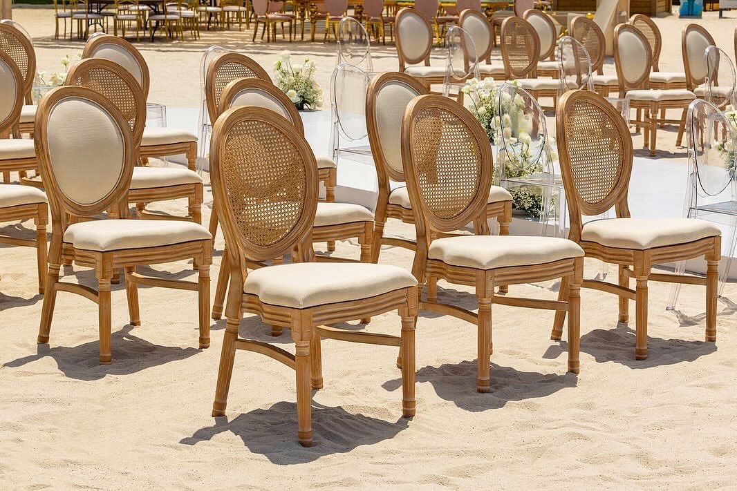 Wooden cane-back chairs and clear acrylic chairs arranged on a sandy beach setting.