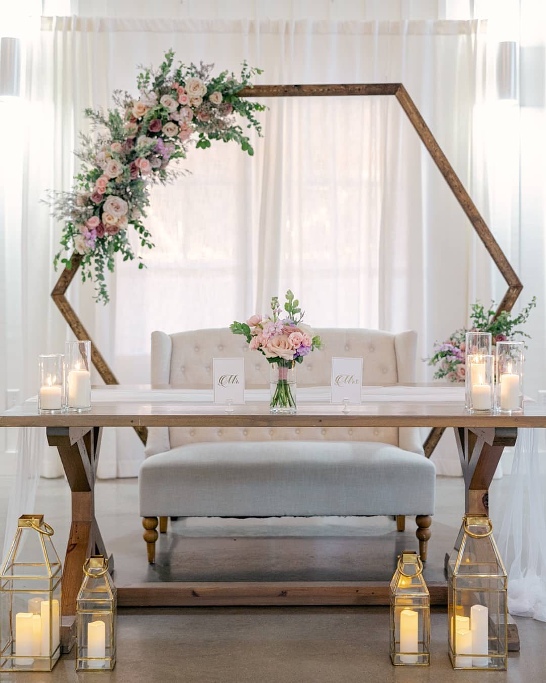 A wooden wedding head table featuring a tufted light blue bench and floral decorations.