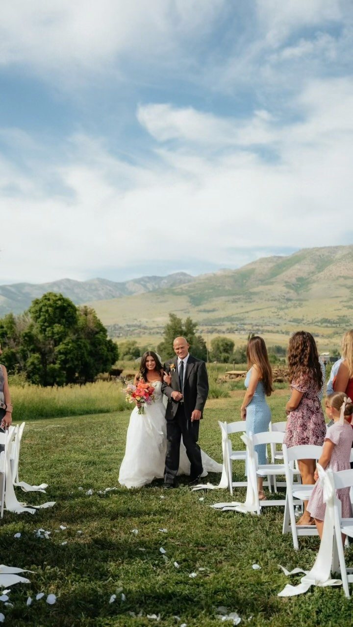 Bride and escort walking down a grassy aisle during an outdoor wedding ceremony.