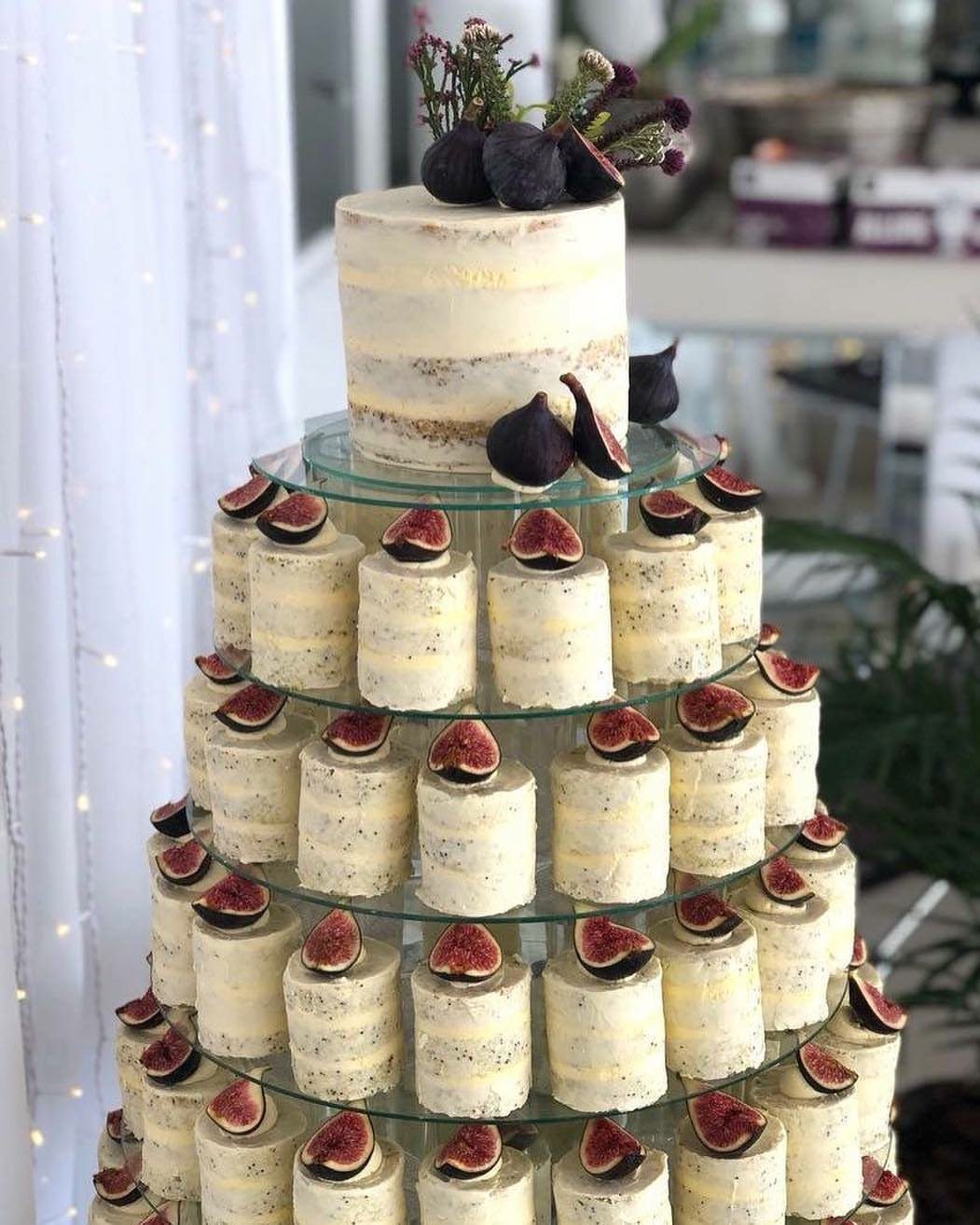 Small individual white frosted cakes topped with sliced figs on a tiered glass stand.