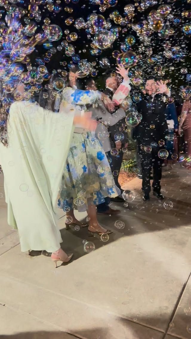Iridescent bubbles floating in the air during an outdoor evening celebration with people in formal wear.