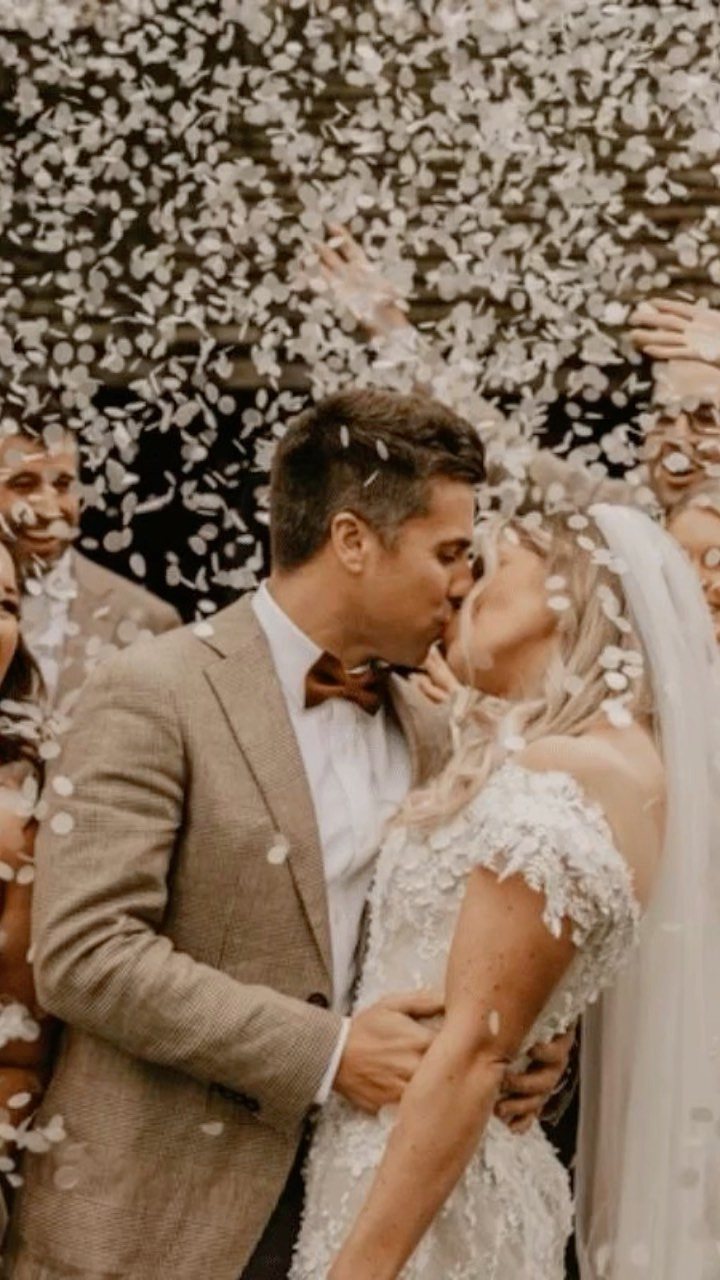 A bride and groom kissing while white confetti falls all around them during their wedding celebration.