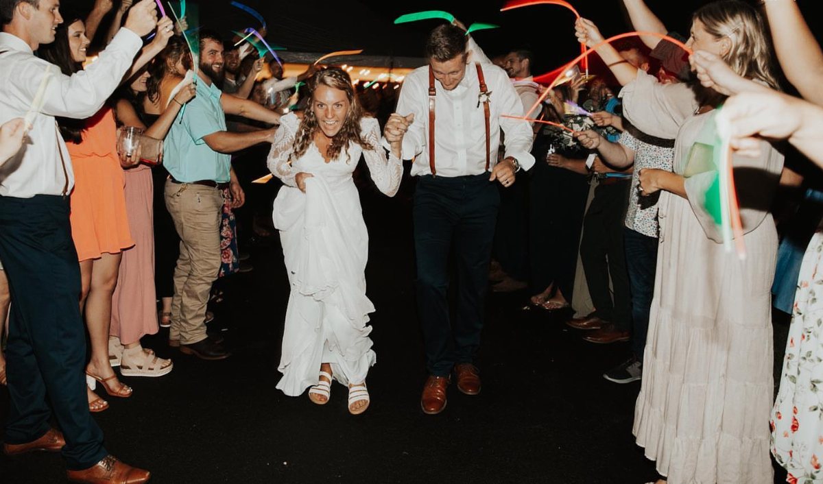 Newlyweds running through a tunnel of guests holding colorful glowing sticks at night.