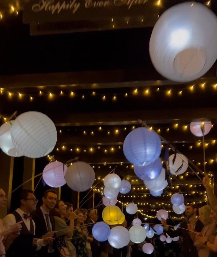 People holding glowing paper lanterns on sticks during a nighttime wedding celebration.