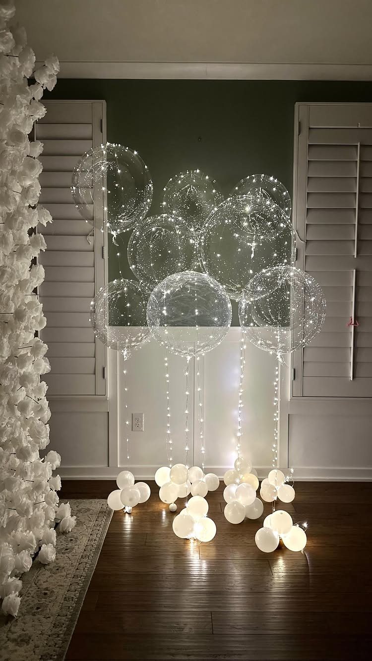 Clear transparent balloons with internal lights arranged above glowing white orb balloons on a wooden floor.